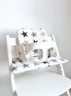 a white wooden rocking chair with black and white stars on the seat cover, against a white wall