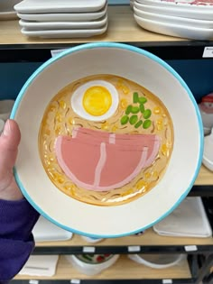 a person holding up a bowl of ramen with an egg and meat in it