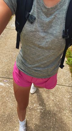 a woman wearing pink shorts and a gray shirt is standing on a sidewalk with her back to the camera