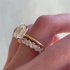 a woman's hand holding an engagement ring with three stones on the band and a diamond in the middle