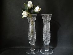 two clear vases with white flowers in them on a black tableclothed surface