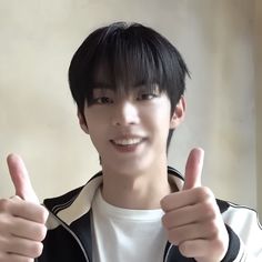 a young man giving the thumbs up sign with both hands and wearing a black and white jacket