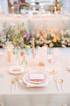 a table set with place settings and flowers in vases, candles and napkins