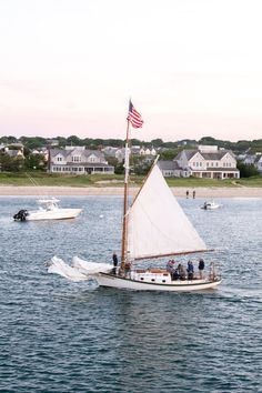 a sailboat with people on it in the water near some houses and an american flag