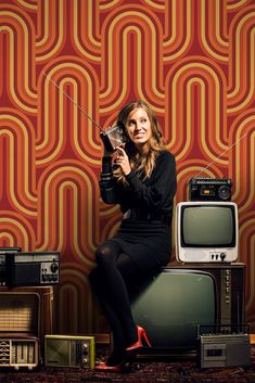 a woman sitting on top of a tv next to an old fashioned radio and other electronics