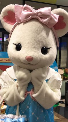 a white stuffed animal with a pink bow on it's head standing in front of a table