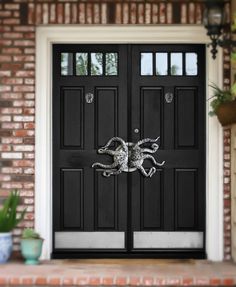 a black front door with an octopus decoration on it's side and two potted plants next to it