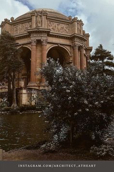 an old building surrounded by trees and water in the middle of a park with clouds overhead