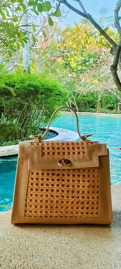 a brown handbag sitting on top of a table next to a pool with trees in the background