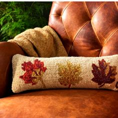 a brown leather chair with a decorative fall leaf pillow on it's back, next to a potted plant