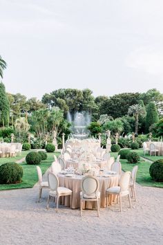 an outdoor dining table set up in the middle of a garden with lots of trees and bushes