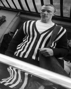 a man standing in front of a mirror wearing a striped sweater and suspender pants