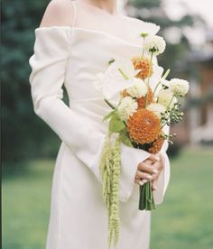 a woman in a white dress holding a bouquet of orange and white flowers on her wedding day