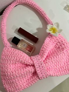 a pink crocheted purse with lipstick, nail polish and a flower on it