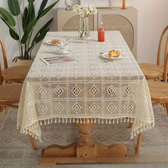 a white table cloth with tassels and plates on it in front of a potted plant