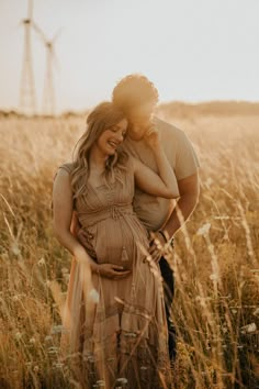 a pregnant couple standing in a field with windmills in the background