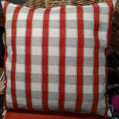 a red and white striped pillow sitting on top of a wooden chair next to a wicker basket