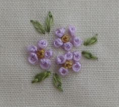 small purple flowers with green leaves on a white cloth background, arranged in the shape of a flower