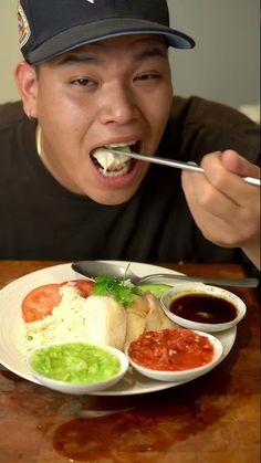 a man eating food from a white plate on top of a wooden table with sauces and condiments