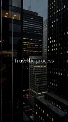 the words trust the process are lit up in front of tall buildings