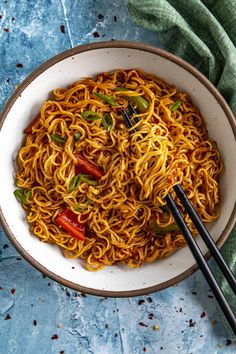 a bowl filled with noodles and chopsticks on top of a blue table cloth