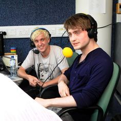 two young men sitting next to each other in front of a computer monitor with headphones on