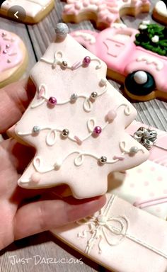 a hand holding some decorated cookies in the shape of christmas trees and cars with bows on them