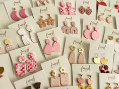 many different types of earrings are displayed on the table with white cards and envelopes