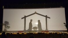 the silhouettes of two people holding hands in front of a large screen at night