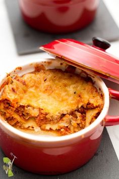 a red casserole dish with cheese and meat in it sitting on a counter