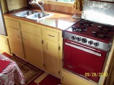 a red stove top oven sitting inside of a kitchen next to a sink and window