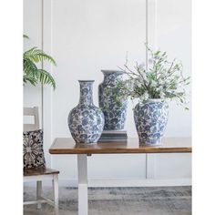 three blue and white vases sitting on top of a table next to a plant