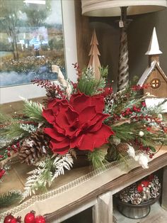 a red flower sitting on top of a mantle covered in pine cones and greenery