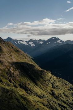 the mountains are covered with green grass and snow capped peaks, as seen from above