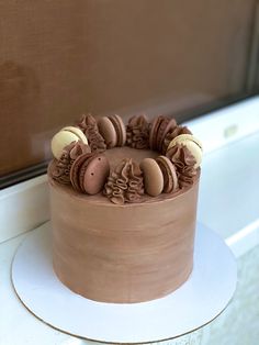 a chocolate cake sitting on top of a white plate next to a window sill