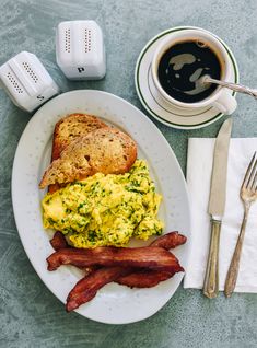 a plate with eggs, bacon and toast on it next to a cup of coffee