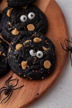 cookies decorated with eyes and sprinkles are on a wooden plate next to a spider