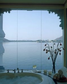 a bath tub sitting next to a large window overlooking the water and buildings in the distance