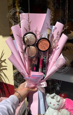 a person holding up a pink bouquet filled with makeup and other items in front of a store window