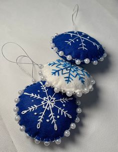 three snowflake ornaments hanging from strings on a white tablecloth with beads and thread