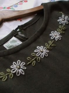 a green sweater with white flowers on it and a wooden hanger next to it