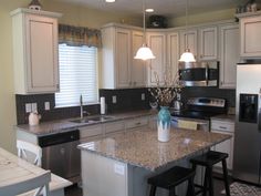 a kitchen with white cabinets and granite counter tops, black appliances and an island in the middle