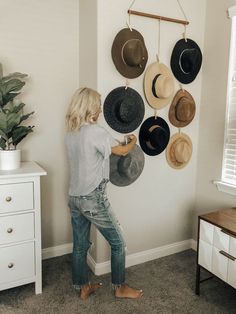 a woman standing in front of a wall with hats hanging on it