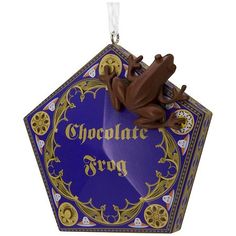 a chocolate frog ornament hanging from a string on a white background with the words chocolate frog in gold lettering