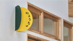 a yellow and green clock mounted to the side of a white wall next to windows