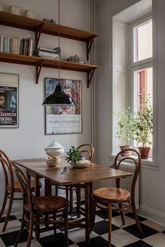 a dining room table and chairs with bookshelves above it, in front of a window