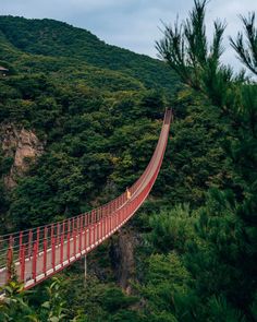 a red suspension bridge over a river in the mountains