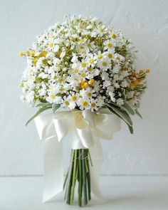 a bouquet of daisies and other flowers in a white ribbon tied around the stems