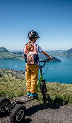 a young boy on a scooter looking out over the water from atop a hill