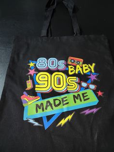 "80's Baby, 90's Made Me This colorful black bag will be the talk wherever you go. Tote bags for any occasion. I have the bag that you have been looking for.  This 100% cotton bag come in one size-13.5\" x 13.5\"-this is perfect for the everyday use. The canvas material will showcase the design in a great color, and it is durable and will last for years.  The bag has a 20\" handles that is made of the same material of the bag.  Care Instructions: Machine was cold. Do not bleach. Tumble dry low. Do not iron directly over the printed area. If iron is needed place butcher paper over area and let completely cool. Do not dry clean" Casual Black Bags With Graphic Design, Black Cotton Canvas School Bag, Trendy Black Cotton Canvas Bag, Retro Cotton School Bag, Retro Cotton Bag With Letter Print, Retro Tote Canvas Bag For School, Retro Cotton Bags With Letter Print, Retro Canvas Bags With Letter Print, Vintage Black Canvas Bag For Daily Use